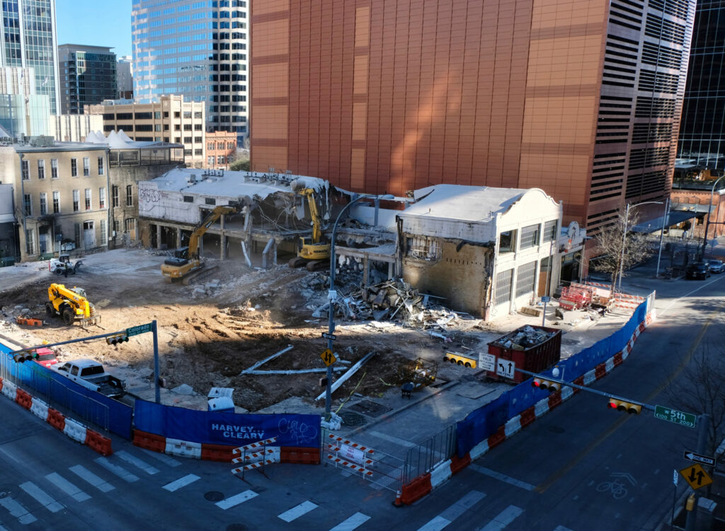 An aerial view of the warehouse-like 409 Colorado building being demolished, multiple excavators tearing through its two stories of concrete and rebar